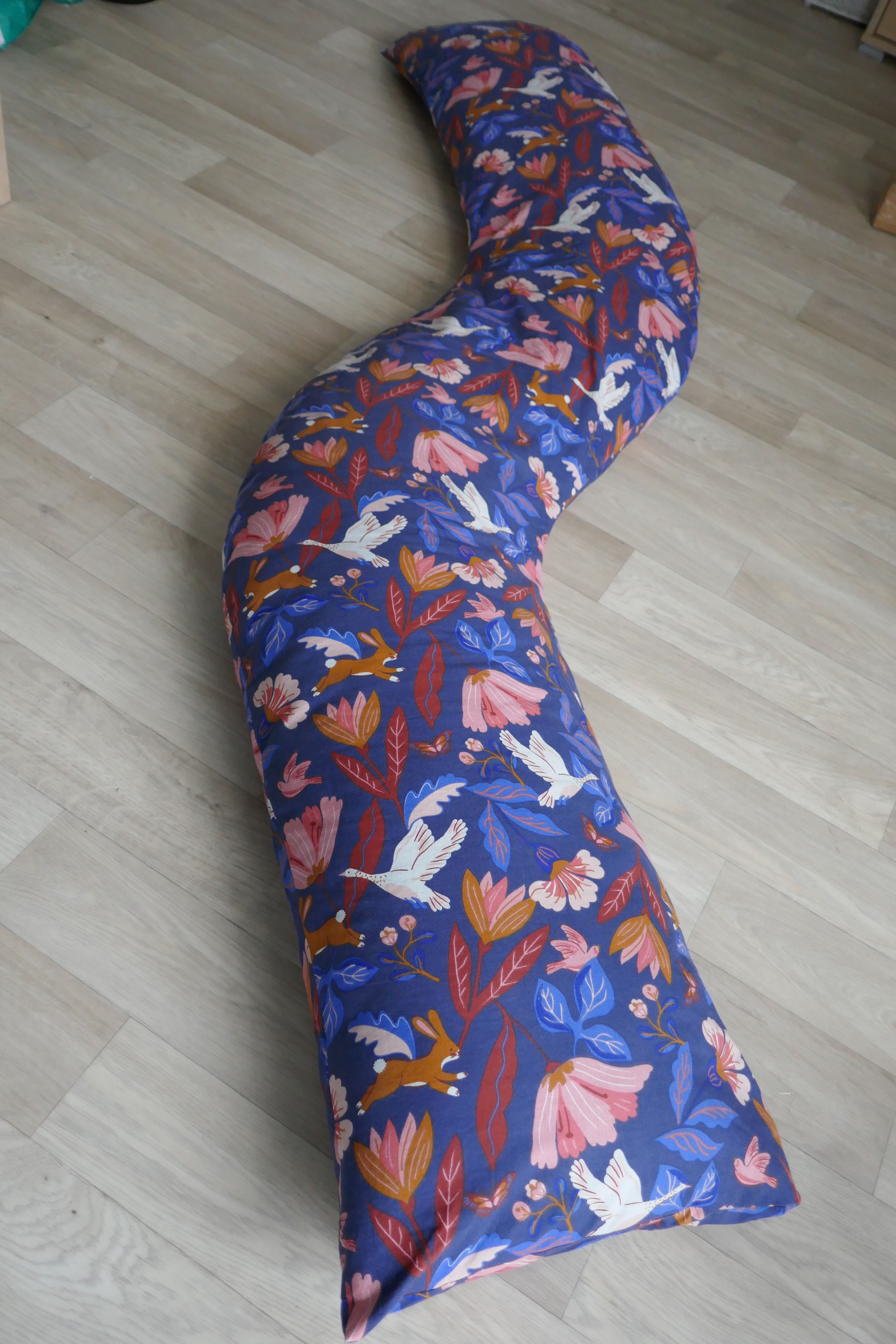  Un coussin en forme de traversin mais coudé sur le sol. Le tissus est bleu foncé avec des oiseaux et des fleurs beiges.