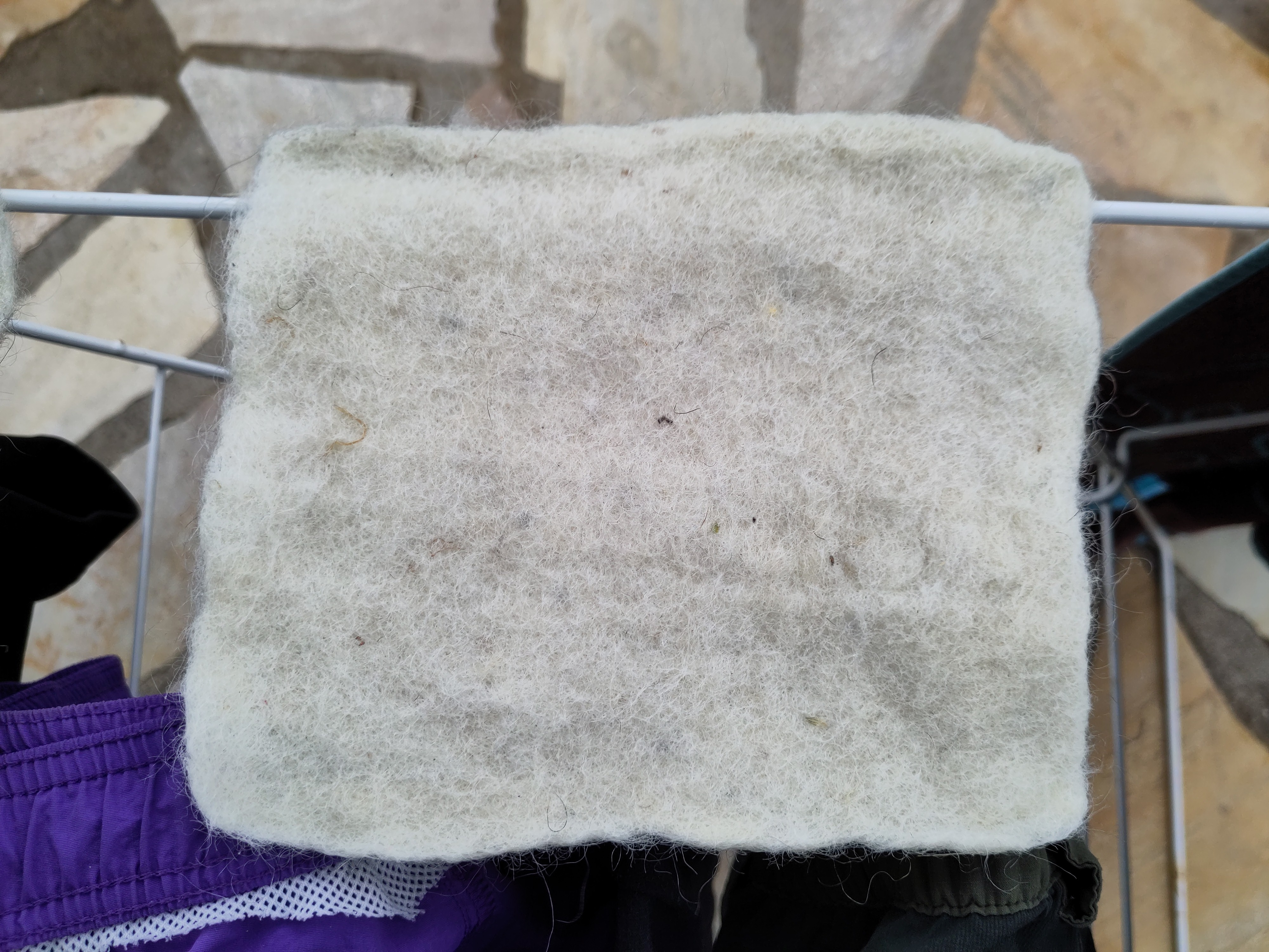 un rectangle plutot propre de laine blanche feutrée, il y a des restes de pailles dans la laine blanche.