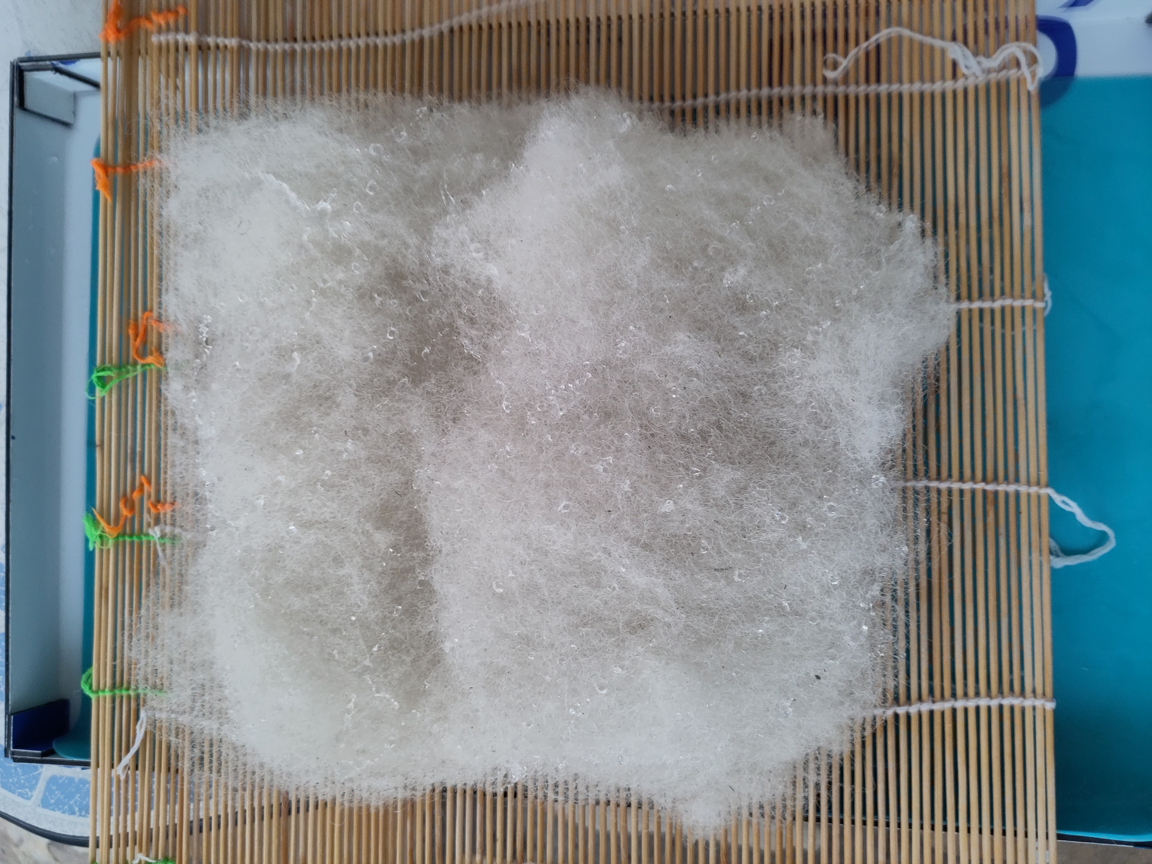 un tas de laine trés fluffy sur une nappe en bambou. le tas est a peu prés carré