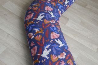 Un coussin en forme de traversin mais coudé sur le sol. Le tissus est bleu foncé avec des oiseaux et des fleurs beiges.